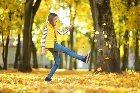 Adorable young girl having fun on beautiful autumn day. Happy child playing in autumn park. Kid gathering yellow fall foliage. Autumn activities for children.の写真素材