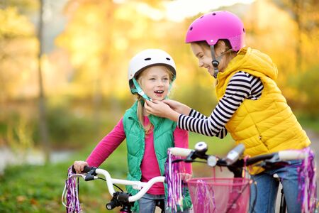Cute little sisters riding bikes in a city park on sunny autumn day. Active family leisure with kids. Children wearing safety helmet while riding a bicycle.の写真素材