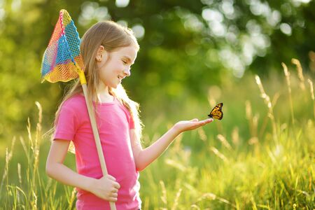 Adorable little girl catching butterflies and bugs with her scoop-net. Child exploring nature on sunny summer day. Family leisure with kids at summer.の写真素材