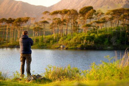 Tourist admiring the view of Twelve Pines Island, standing on a gorgeous background formed by the sharp peaks of a mountain range called Twelve Pins or Twelve Bens, Connemara, County Galway, Irelandの写真素材