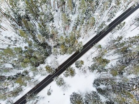 Beautiful aerial view of snow covered pine forests and a road winding among trees. Rime ice and hoar frost covering trees. Scenic winter landscape near Vilnius, Lithuania.の写真素材