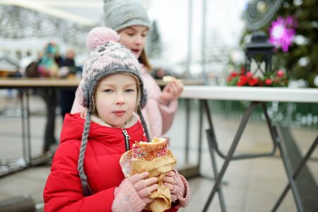 Two cute young sisters eating Czech trdelnik on traditional Christmas fair in Vilnius, Lithuania. Children enjoying sweets, candies and gingerbread on Xmas market. Winter time with family and kids.の写真素材