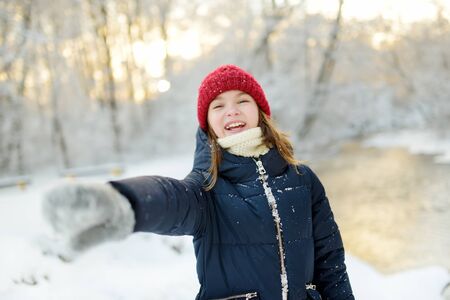 Adorable young girl having fun in beautiful winter park during snowfall. Cute child playing in a snow. Winter activities for family with kids.の写真素材