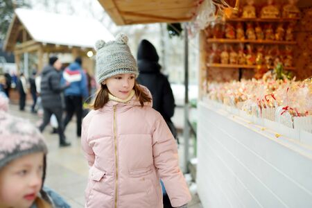Young girl looking at Christmas dolls and decorations sold at Christmas market in Vilnius, Lithuania. Decorated and illuminated shopping stands with variety of Xmas toys.の写真素材