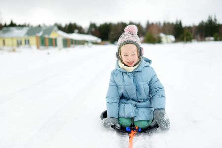 Funny little girl having fun with a sleigh in beautiful winter park. Cute child playing in a snow. Winter activities for kids.の写真素材