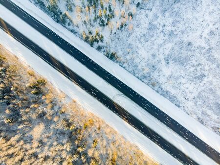 Beautiful aerial view of snow covered fields with a two-lane road among trees. Rime ice and hoar...
