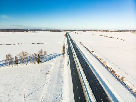 Beautiful aerial view of snow covered fields with a two-lane road among trees. Rime ice and hoar frost covering trees. Scenic winter landscape near Vilnius, Lithuania.の写真素材