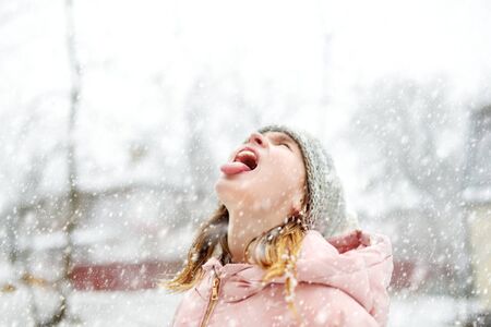 Adorable young girl catching snowflakes with her tongue in beautiful winter park. Cute child playing in a snow. Winter activities for kids.の写真素材
