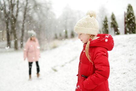 Two adorable young girls having fun together in beautiful winter park. Cute sisters playing in a snow. Winter activities for family with kids.の写真素材