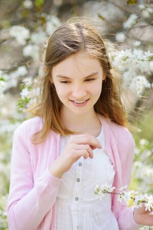 Adorable little girl in blooming apple tree garden on beautiful spring day. Cute child picking fresh...