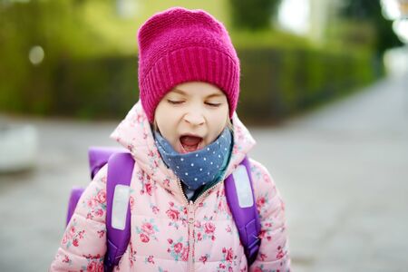 Cute sleepy little girl yawning on her way to school. Child with a backpack in a morning. Education...