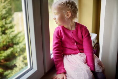 Adorable little girl looking through the window at homeの写真素材