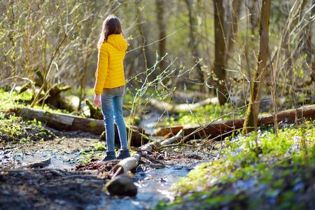 Cute young girl having fun by a river on warm spring day. Child playing by a water. Outdoor family activities in early spring.の写真素材