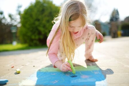 Cute little girl drawing with colorful chalks on a sidewalk. Summer activity for small kids. Creative leisure for family.の写真素材