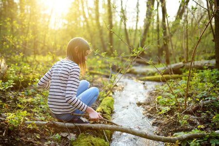 Cute young girl having fun by a river on warm spring day. Child playing by a water. Outdoor family activities in early spring.の写真素材