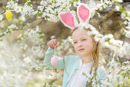 Adorable little girl wearing bunny ears in blooming cherry garden on beautiful spring day. Kid...