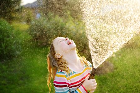 Adorable little girl playing with a garden hose on warm summer day. Child having fun with water on hot day. Outdoor summer activities for kids.の写真素材