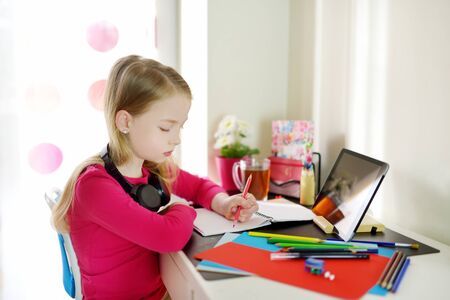 Young schoolgirl doing her homework with digital tablet at home. Child using gadgets to study. Education and distance learning for kids. Homeschooling during quarantine. Stay at home entertainment.の写真素材