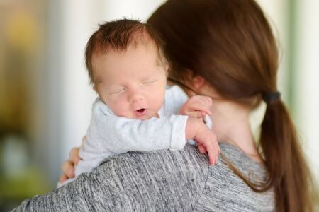 Cute little newborn baby boy in his mothers arms. Portrait of tiny new baby at home. Adorable son...
