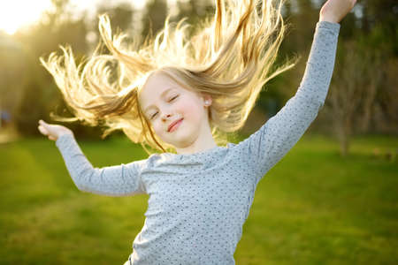 Cute little girl having fun outdoors on sunny summer evening. Child exploring nature. Summer activities for kids.の写真素材