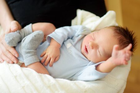 Cute little newborn baby boy sleeping in his mothers arms. Portrait of tiny new baby at home. Adorable son being held by his mommy. New bundle of joy.の写真素材