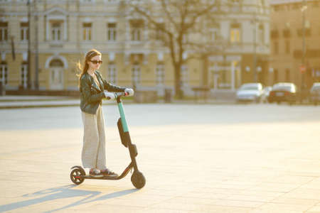Cute young girl riding an electric scooter on warm and sunny spring day. Electric urban transportation in Vilnius, Lithuania. Scooters for rent. Family leisure with kids.の写真素材