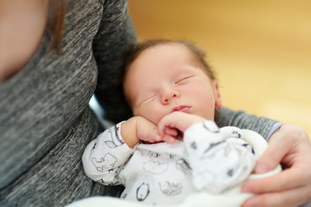 Cute little newborn baby boy sleeping in his mothers arms. Portrait of tiny new baby at home....