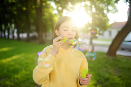 Pretty teenage girl blowing soap bubbles on a sunset. Child having fun in a park in summer. Funny...