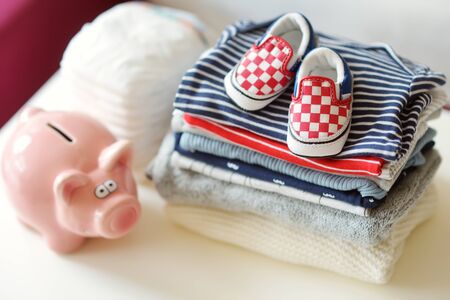 A pile of baby clothes, disposable diapers and a piggy bank. Parenting expenses concept. Working out a baby budget. Saving money when planning for a newborn. Budgeting for a new baby.の写真素材