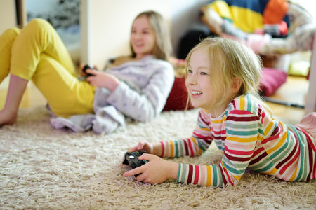 Two sisters playing video games at home. Children having fun together holding gaming controllers....