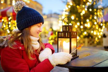 Cute young girl looking at a lantern on traditional Christmas fair in Riga, Latvia. Children enjoying sweets, candies and gingerbread on Xmas market. Winter time with family and kids.の写真素材