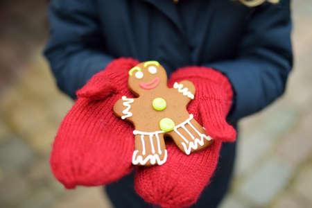 Cute young girl having gingerbread cookie on traditional Christmas fair in Riga, Latvia. Child enjoying sweets, candies and gingerbread on Xmas market. Winter time with family and kids.の写真素材