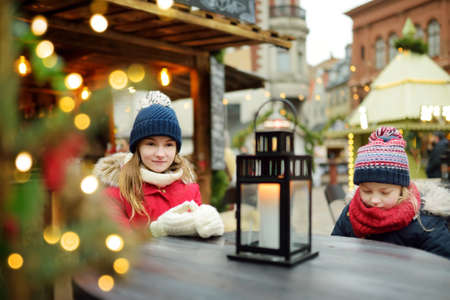 Two adorable sisters sitting having fun together on traditional Christmas fair in Riga, Latvia. Winter time with family and kids.の写真素材