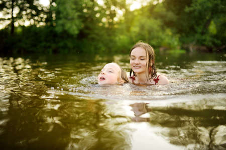 Two young sisters having fun on a sandy lake beach on warm and sunny summer day. Kids playing by the...