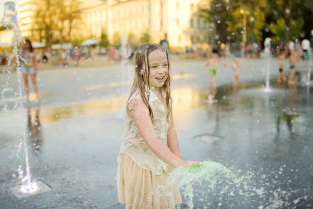 Cute young girl playing in fountains on newly renovated Lukiskes Square in Vilnius, Lithuania. Child having fun with water on sunny summer day. Active leisure for kids.の写真素材