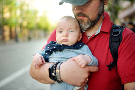 Cute little baby boy in his fathers arms. Dad and son having fun on sunny summer day in city park....