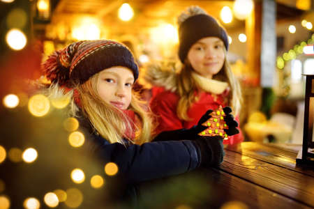 Two adorable sisters having a good time together on traditional Christmas fair in Riga, Latvia. Children enjoying sweets, candies and gingerbread on Xmas market. Winter time with family and kids.の写真素材