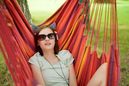 Happy young girl relaxing in hammock on beautiful summer day. Cute child having fun in summer park. Family leisure at summer.の写真素材