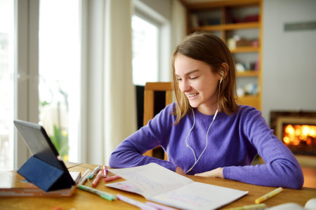 Preteen schoolgirl doing her homework with digital tablet at home. Child using gadgets to study....