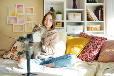 Beautiful teenage girl recording video blog with her smartphone. Young vlogger shooting vlog at home. Teen influencer creating content for her social media account. Social media and blogging concept.の写真素材