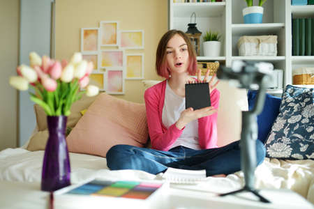 Beautiful teenage girl recording video blog with her smartphone. Young vlogger shooting vlog at home. Teen influencer creating content for her social media account. Social media and blogging concept.の写真素材