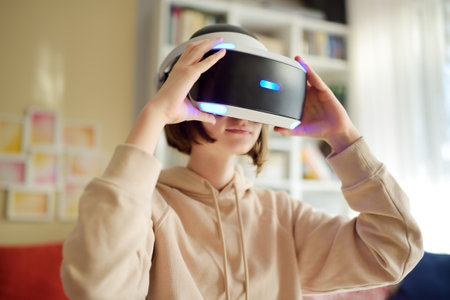 Pretty teenage girl wearing virtual reality headset at home. Cute teen using VR glasses to play a game. Child in virtual augmented reality helmet. Future technology concept.の写真素材