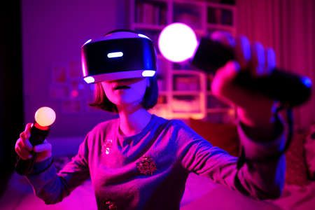 Pretty teenage girl wearing virtual reality headset in a dark room. Cute teen using VR glasses to...