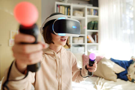 Pretty teenage girl wearing virtual reality headset at home. Cute teen using VR glasses to play a...