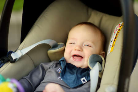 Sweet baby boy smiling happily in a car seat. Infant being carried in a car seat. Family leisure...