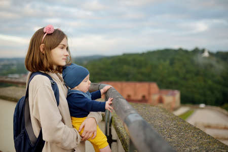 Cute teenage girl holding her baby brother while enjoying a view of Vilnius city from the Gediminas hill. Exploring tourist attractions with kids. Vilnius, Lithuaniaの写真素材