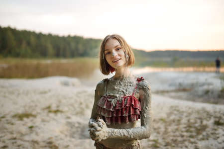 Young girl taking healing mud baths on lake Gela near Vilnius, Lithuania. Child having fun with mud. Kid playing with medicinal clay.の写真素材