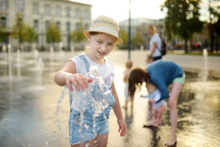 Cute young girl playing in fountains on newly renovated Lukiskes Square in Vilnius, Lithuania. Child having fun with water on sunny summer day. Active leisure for kids.の写真素材