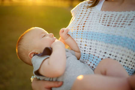 Cute little baby boy in his mothers arms. Mom and son having fun on sunny summer day in city park....