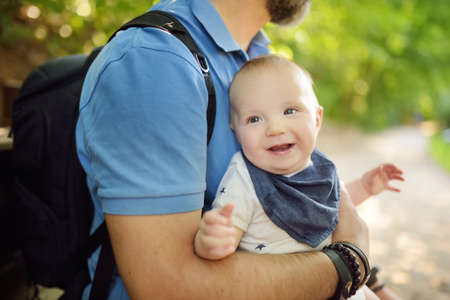 Cute little baby boy in his fathers arms. Dad and son having fun on sunny summer day in city park. Adorable son being held by his daddy.の写真素材